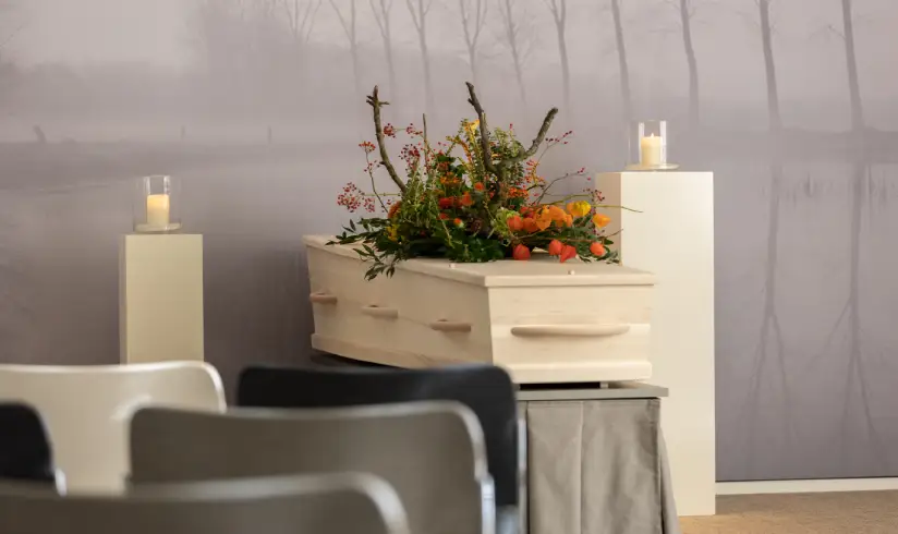 Ruimte met uitvaartkist met bloemen en stoelen op de voorgrond
