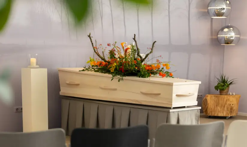Ruimte met uitvaartkist met bloemen en stoelen op de voorgrond