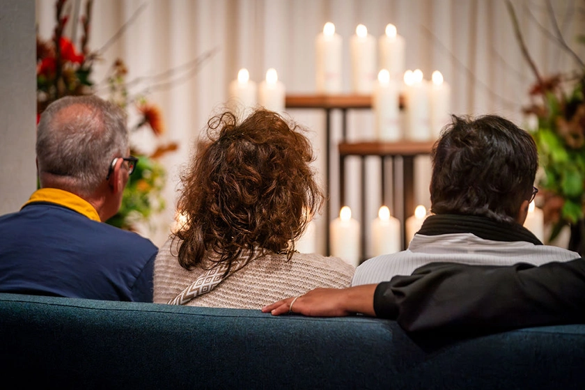 Drie nabestaanden zittend op bank kijkend naar de November 2 Remember aangestoken kaarsen