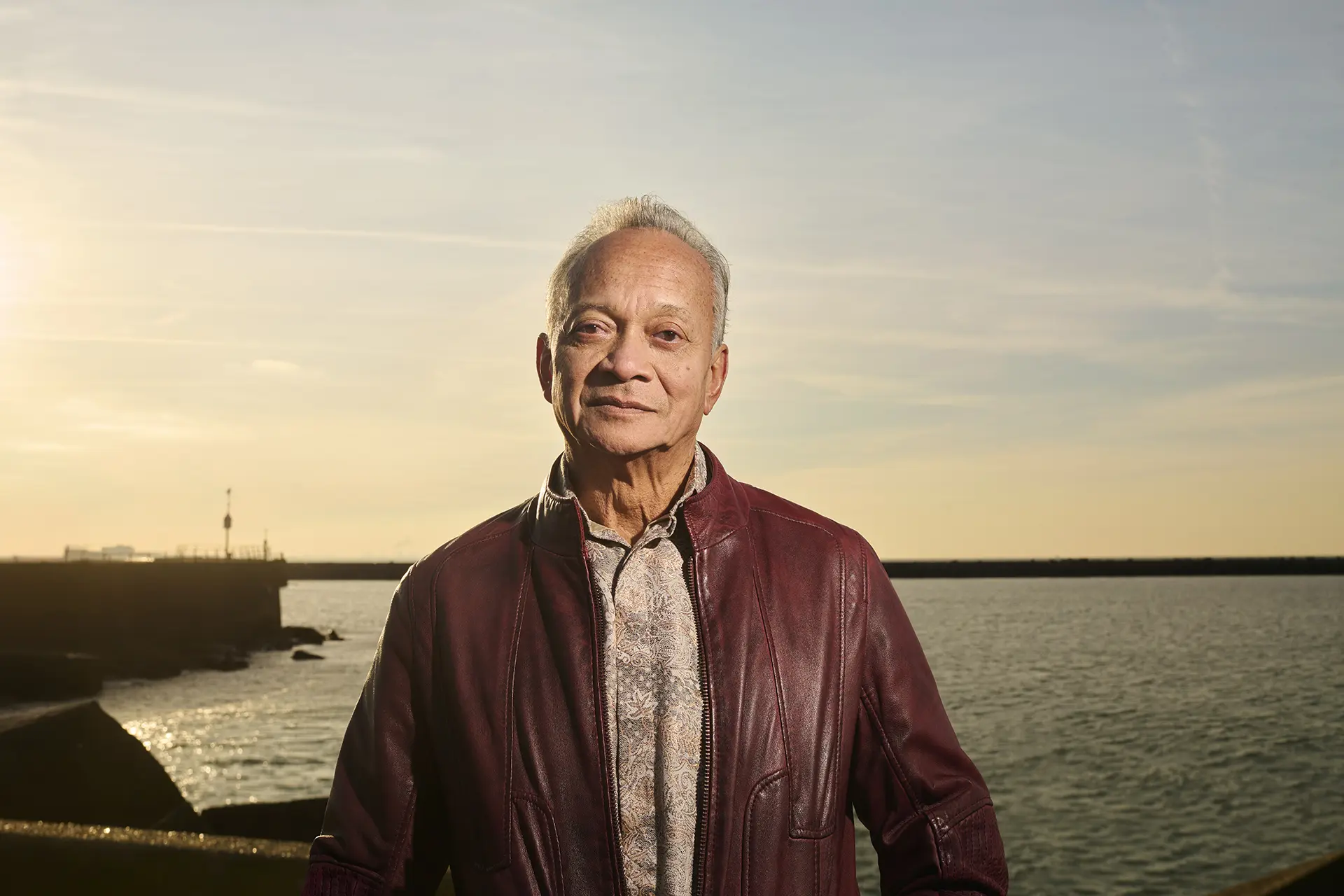 Portretfoto oudere man kijkend in camera met zee op de achtergrond