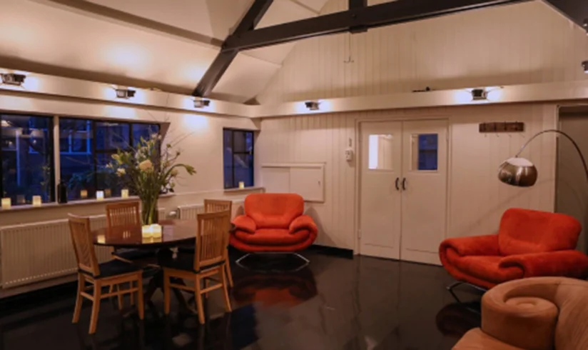 Een kamer met een tafel en stoelen en 2 grote rode fauteuils