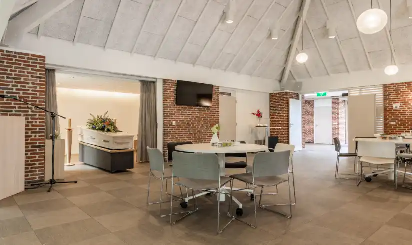 Ruimte met tafels en stoelen en een uitvaartkist met bloemen