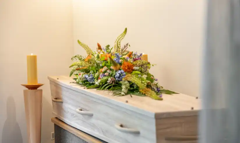 Kamer met uitvaartkist met bloemen en een grote gele kaars