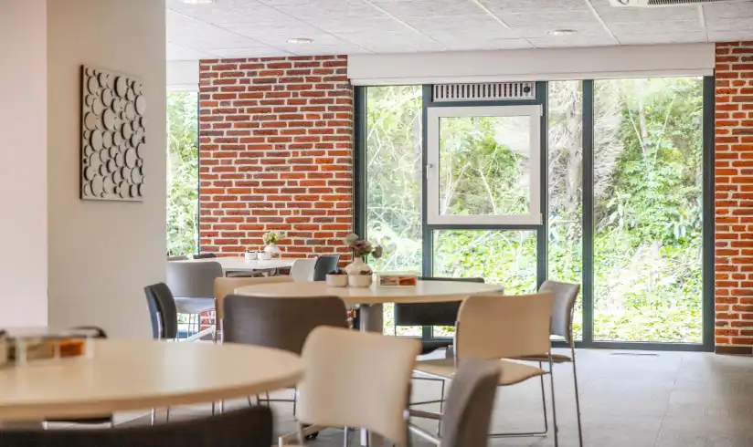Ruimte met 2 tafels met stoelen en grote ramen op de achtergrond