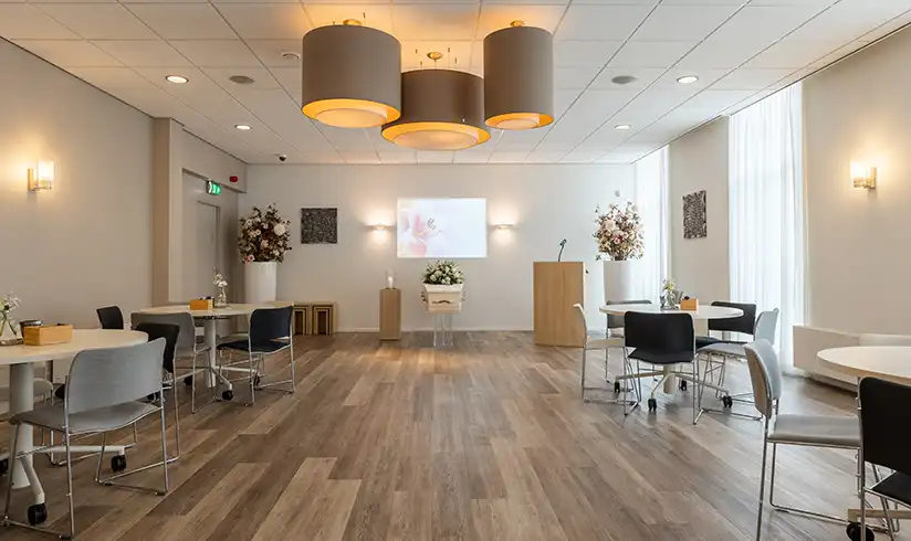 Aula met kist achterin en stoelen en tafels