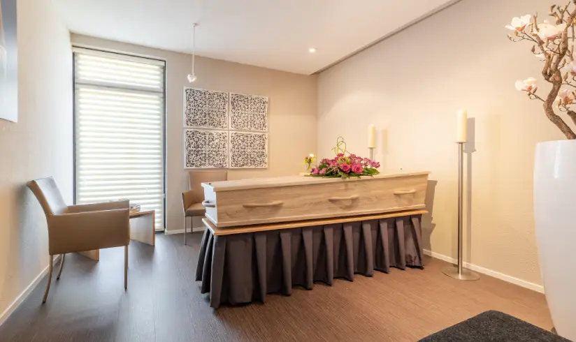 Kamer met uitvaartkist met bloemen en een stoel bij de muur