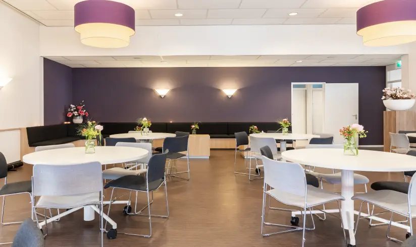 Grote ruimte met tafels en stoelen en een paarse muur achterin
