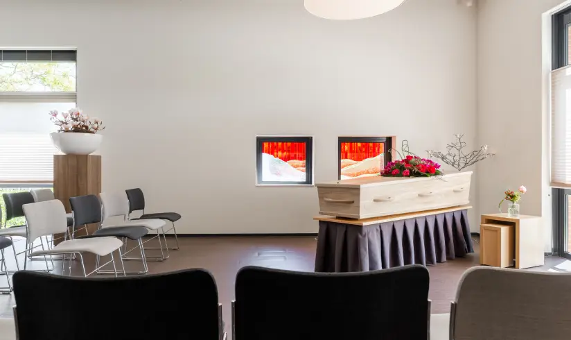 Grote ruimte met een uitvaartkist met bloemen en rijen stoelen