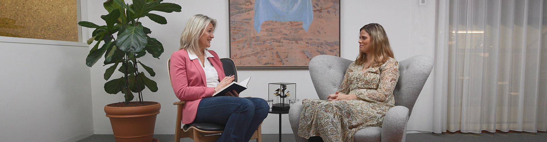 Suzan en Romy zitten tegenover elkaar in stoelen en kijken elkaar aan